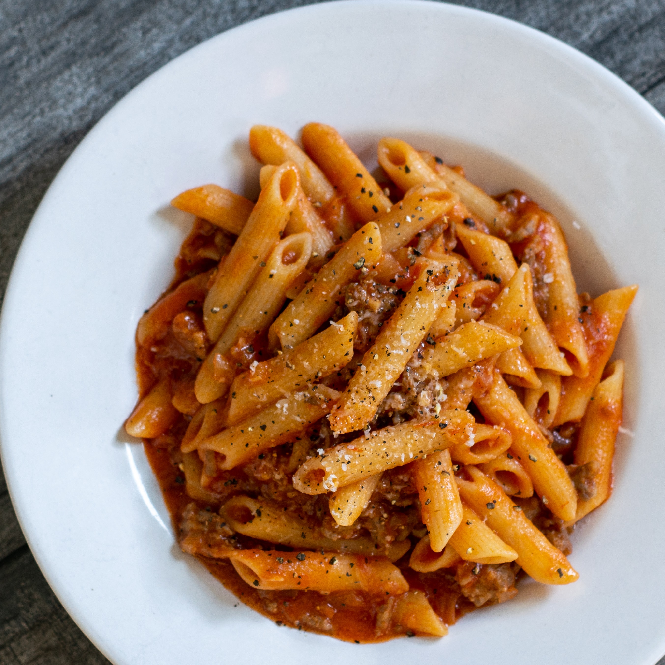 A bowl of rustic penne pasta mixed with a red sauce