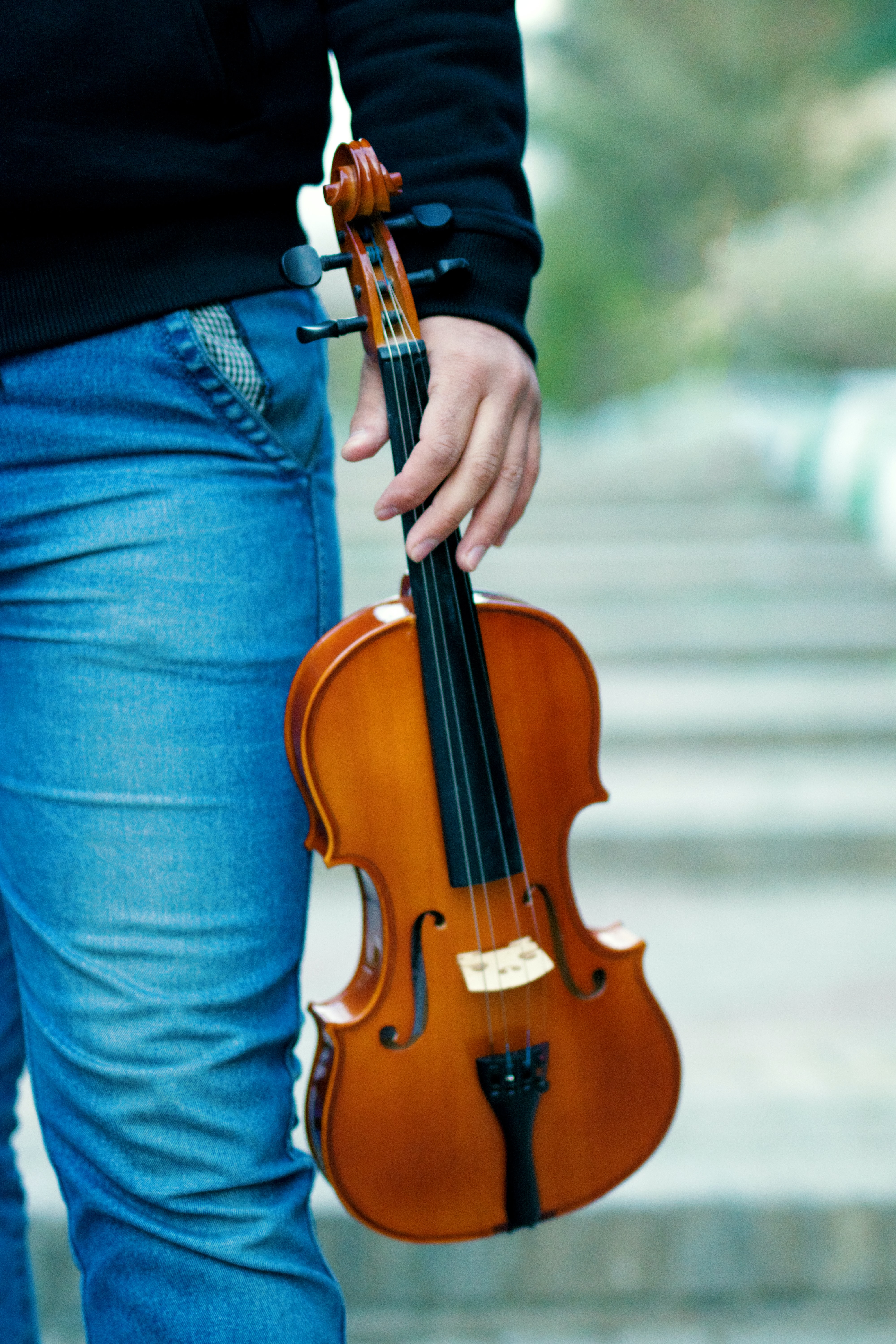 Man in jeans holding a brown fiddle outside