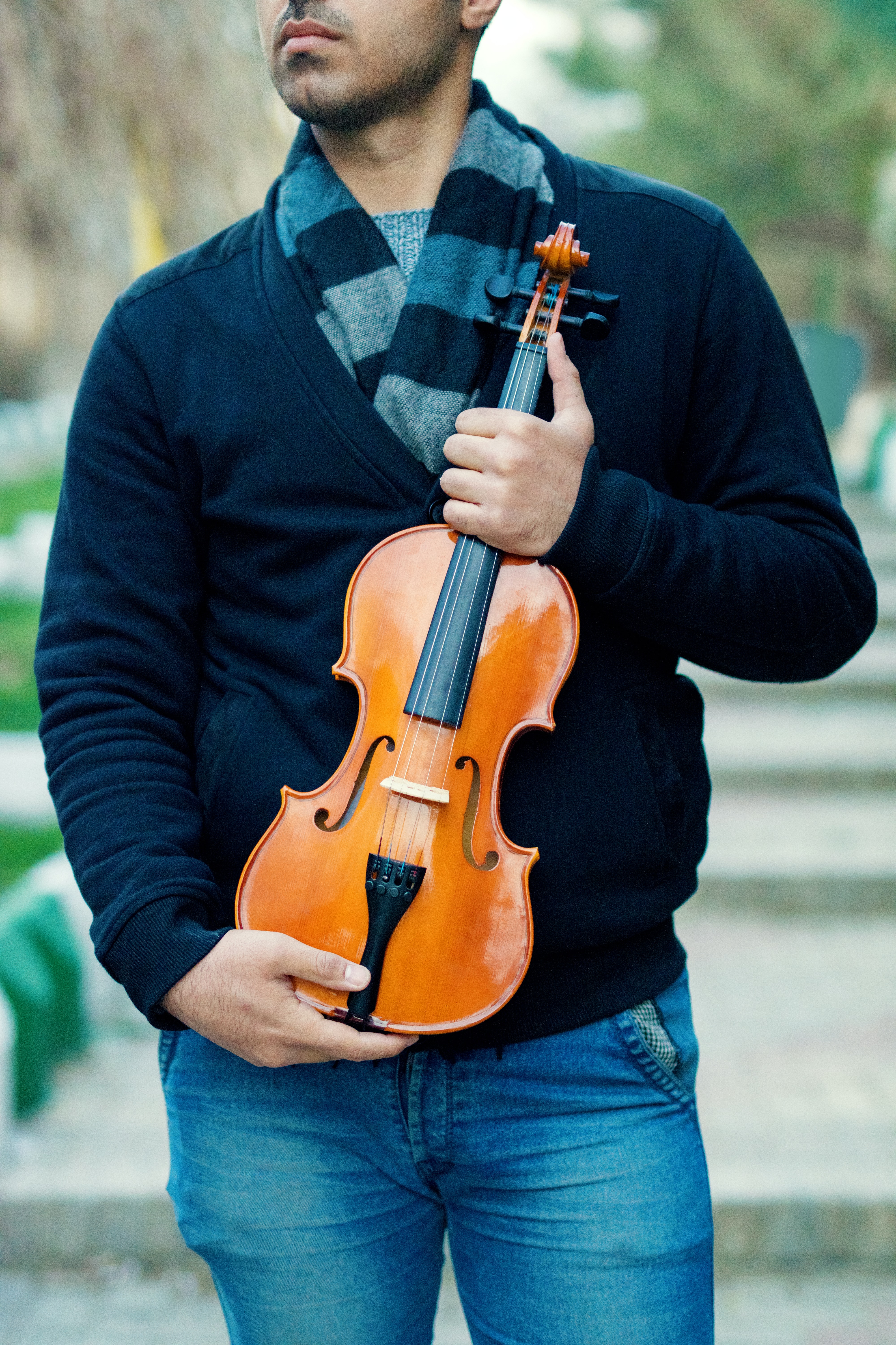 Man wearing a scarf and holding a brown fiddle outside