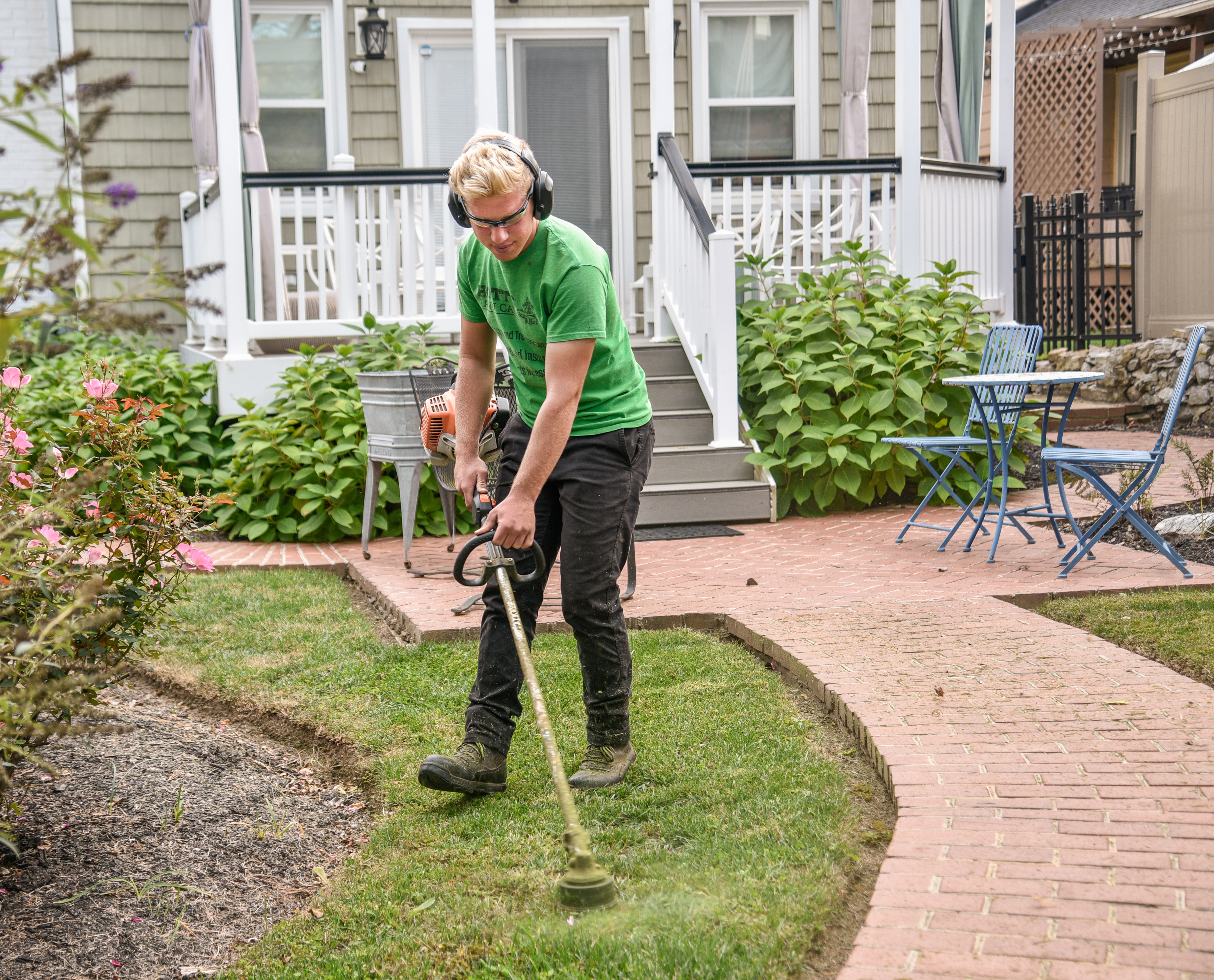 Man in green shirt using a string trimmer in his yard