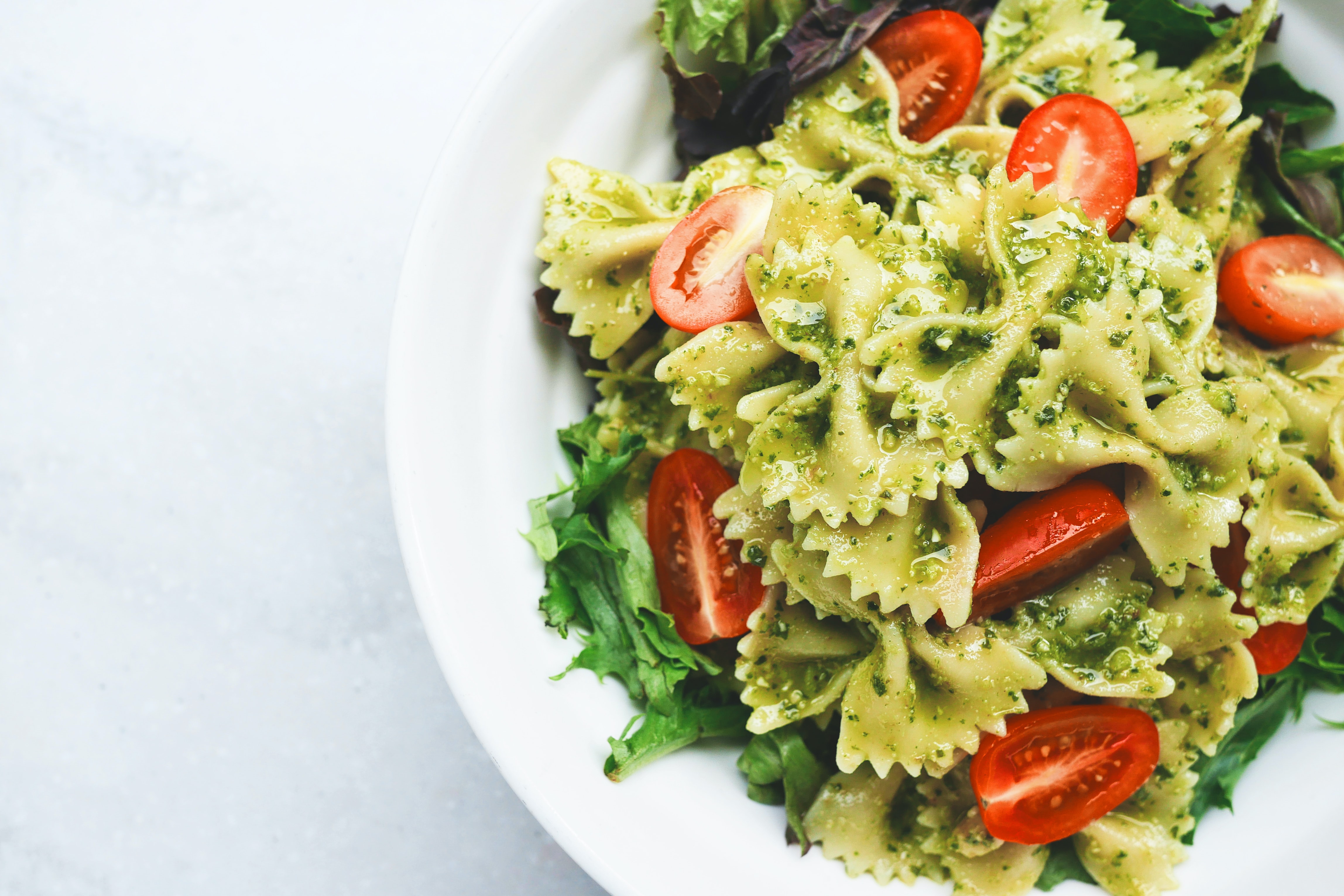 A bowl of pesto bowtie pasta topped with sliced tomatoes